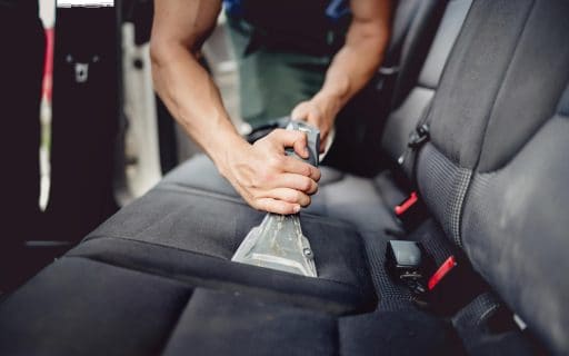 Hands of auto detailer deep cleaning car seat to remove odors