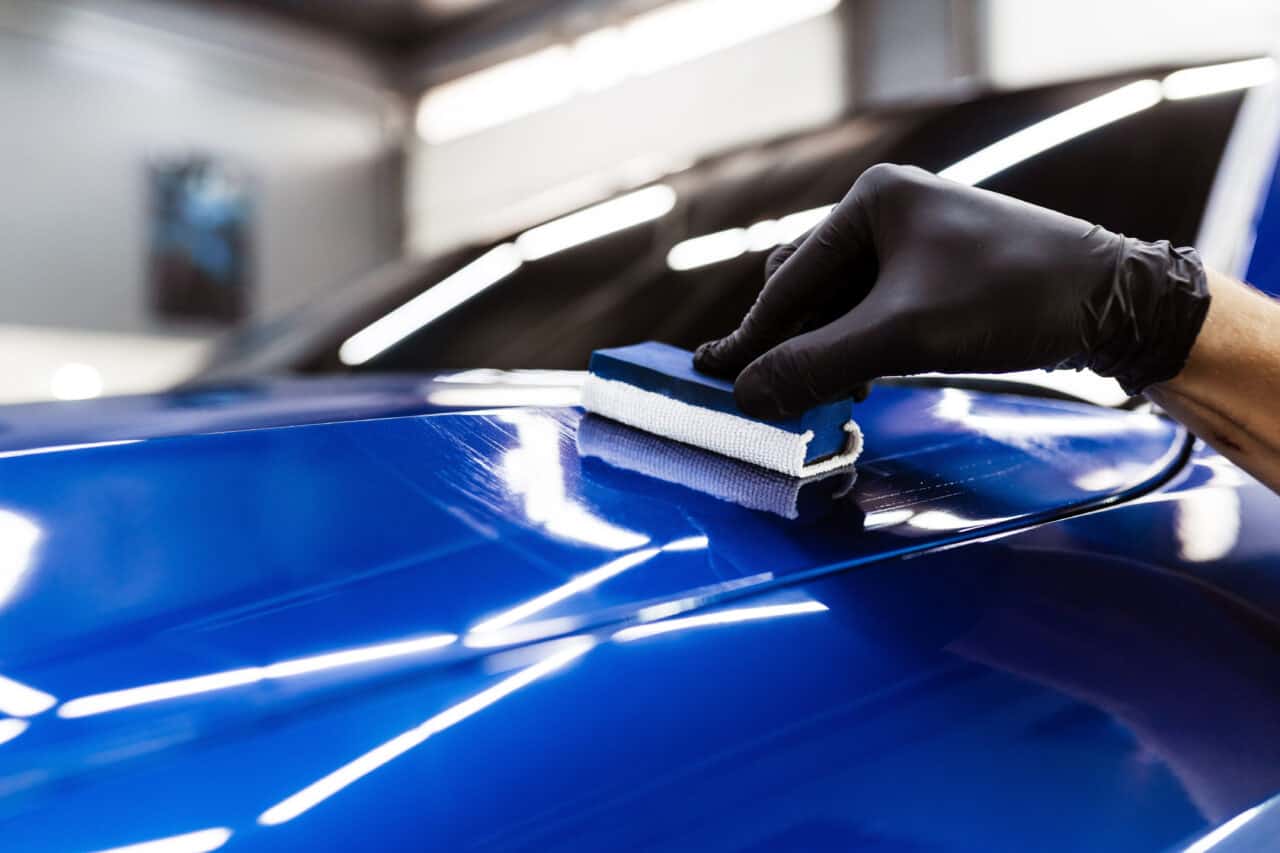 Process of applying ceramic protective coat on body car in detailing auto service. Car service worker apply ceramic coating to protect the car body from scratches.